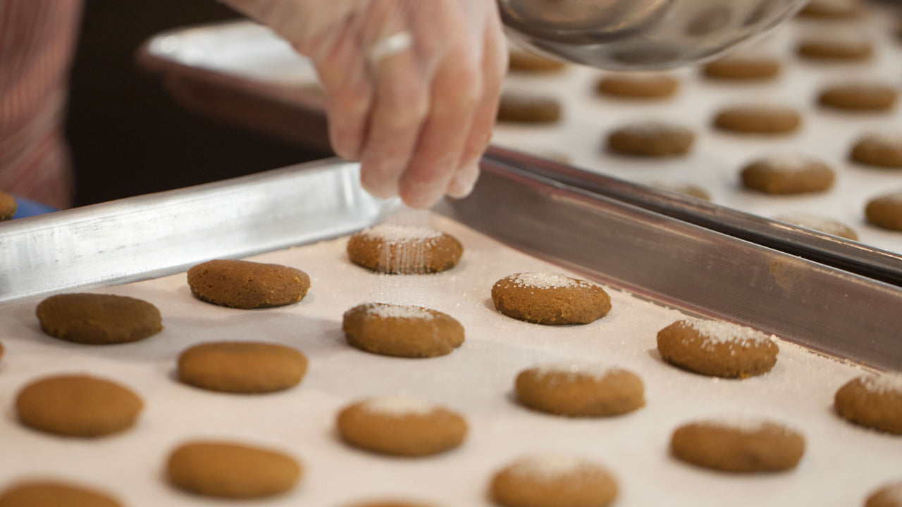 Ginger Cookies on a cookie sheet being sprinkled with sugar before they are baked.
