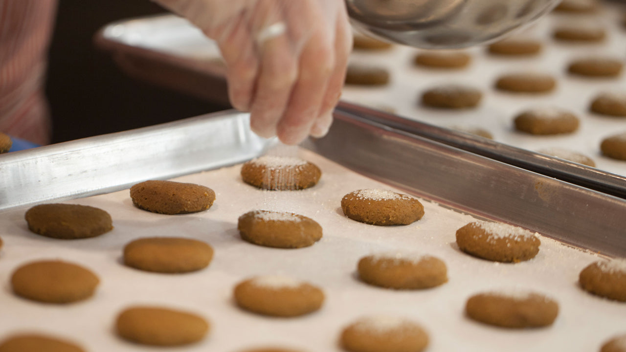Ginger Cookies on a cookie sheet being sprinkled with sugar before they are baked. 