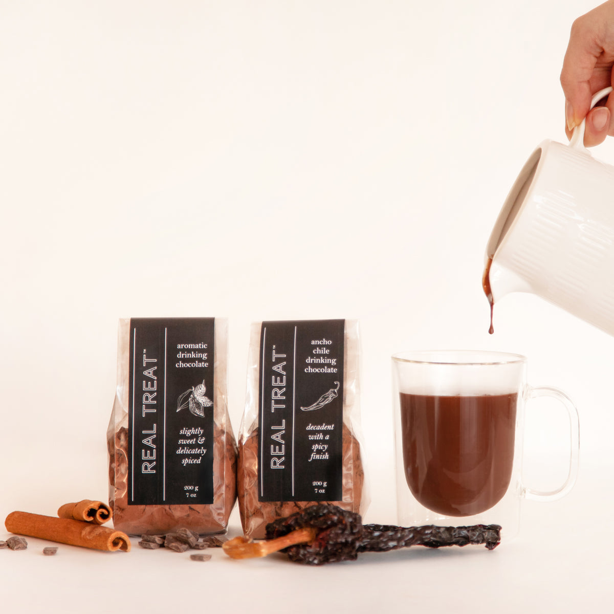 Packages of Ancho Chile Drinking Chocolate and Aromatic Drinking Chocolate  with a clear mug filling with decadent chocolate