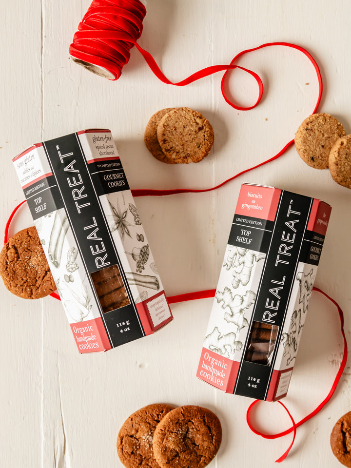 Real Treat organic ginger cookies and spiced pecan shortbread on a table with red ribbon. 