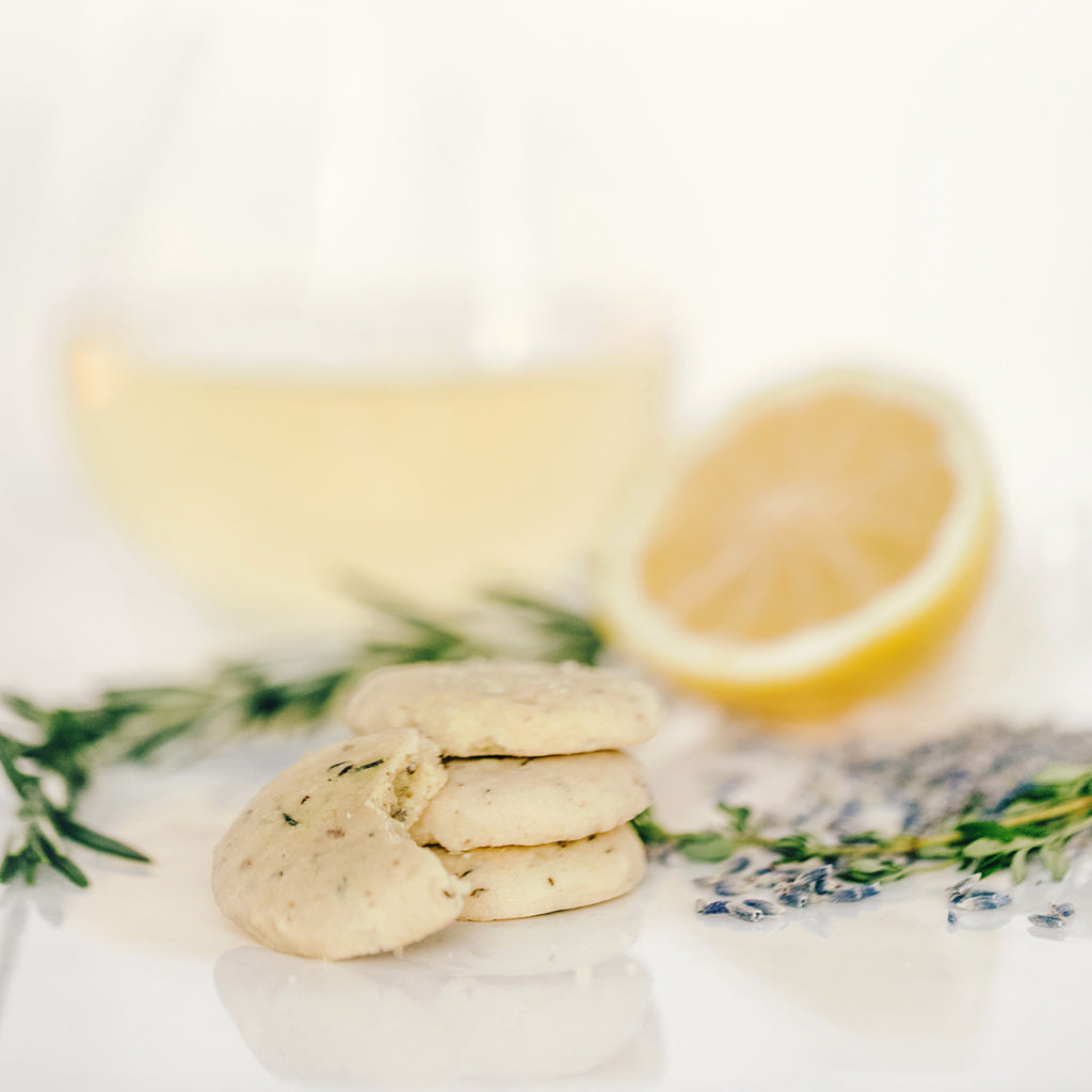 A stack of Lemon Sablés with Herbes de Provence next to a glass of white wine and a fresh lemon, thyme and lavender.