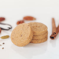 A stack of Spiced Pecan Shortbread next to cinnamon sticks, vanilla bean, and cardamom