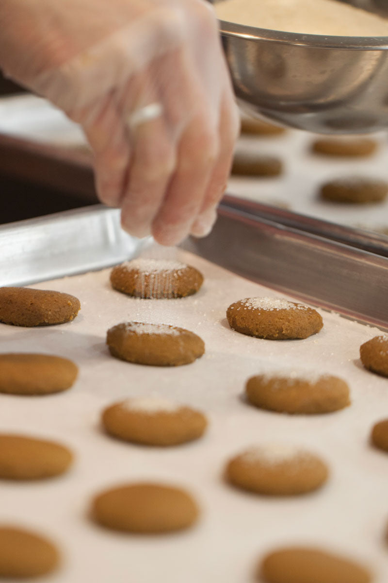 Ginger Cookies on a cookie sheet being sprinkled with sugar before they are baked. 