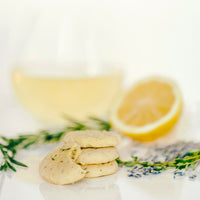 A stack of Lemon Sablés with Herbes de Provence next to a glass of white wine and a fresh lemon, thyme and lavender.